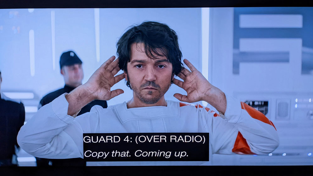 AndorS01E08_10 Cassian Andor in Narkina 5 prison scrubs at a guard station, his hands on his head, looking dull